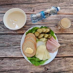 Zdjęcie przedstawia dietę podstawową Chleb mieszany pszenno-żytni Masło extra Szynka krucha z pieca wieprzowa Ser mozzarella Ogórek konserwowy Sałata zielona Kawa zbożowa z mlekiem Woda mineralna Makaron na mleku